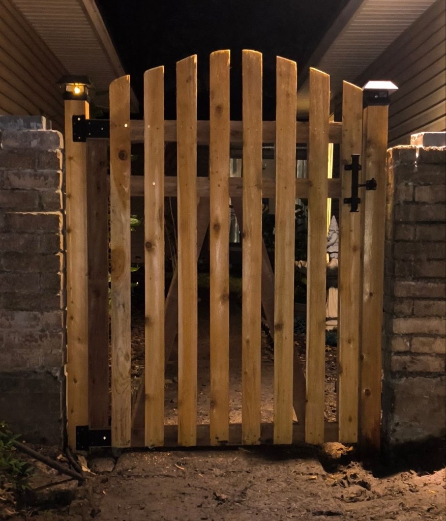 Custom arched cedar gate with black hardware, lit at night